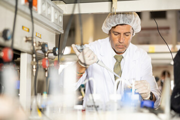 Concentrated Latin man biologist using mechanical lab pipette for mixing chemicals in modern...