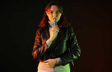 Young woman smoking electronic cigar on dark background