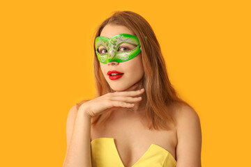 Beautiful young woman in green carnival mask on yellow background