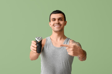 Handsome young man pointing at electric shaver on green background
