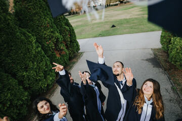 Graduated students in caps and gowns celebrating graduation in a park. They are throwing caps in...