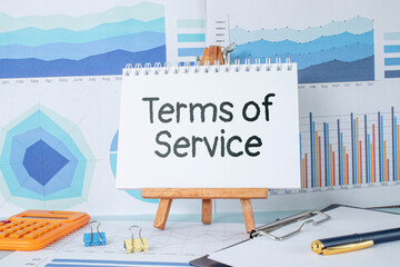 Terms of Service text on a yellow sticker. notepads on a wooden background near a potted plan - obrazy, fototapety, plakaty