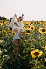 Mother playing with little daughter, lifting her up, in an endless field of sunflowers.