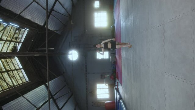 Young female gymnast with muscular tattooed body performing back handspring and backflip in training gym. Vertical format footage