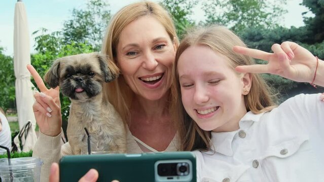 Mother and daughter engage in creation of family selfie capturing happiness reflected in faces. Cute Shih Tsu completes family picture