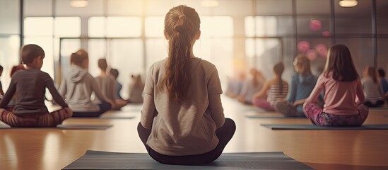 Back view of PE teacher leading Yoga class and meditating with elementary students at school gym. Copy space image. Place for adding text or design