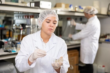 Professional female chemist in uniform examining solution in petri dish while working in research center