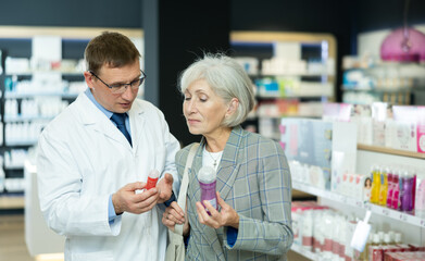 Attentive mature woman choosing lubricant with help of middle-aged male pharmacist in chemist's shop