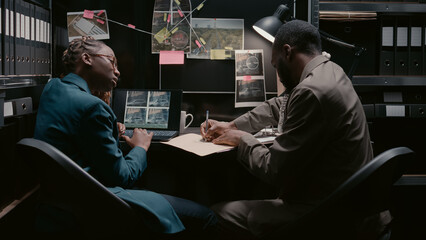 Two police officers analyzing surveillance footage, working on case files for investigation in...