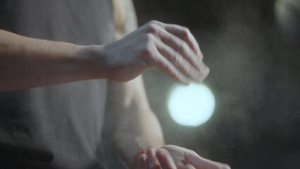 Professional male athlete clapping hands and applying chalk powder to palms while getting ready for gym workout. Close-up view, slow mo