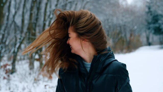 Brunette woman having fun outdoors in winter. Lady waves her long dark hair and smiles happily. Blurred backdrop.