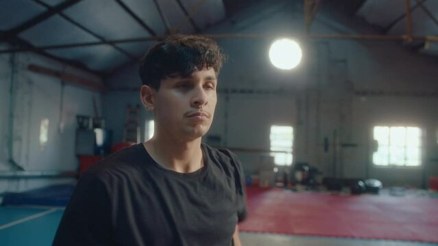 Young male athlete doing arm circles exercise as warming up in training gym before workout. Medium shot