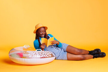 Female model reading book in studio, laying down on inflatable to enjoy lecture novel. Young adult...