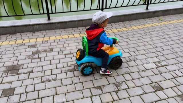 Little Caucasian boy cheerfully riding his toy car. Excited baby on the walk in autumn. Top view.