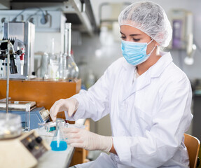 Professional female chemist investigating behavior of blue liquid reagents while working in modern...