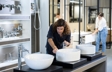 in plumbing department,thoughtful man inspects round white ceramic sinks with faucets.buyer...