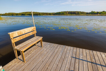 Beautiful view of a wooden bench on a private wooden dock on blue lake dotted with water lilies and...