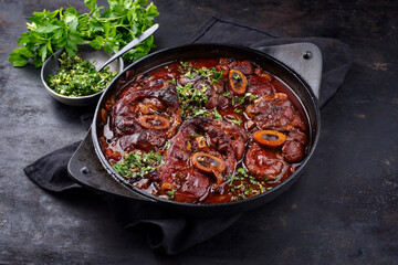 Traditional braised Italian ossobuco alla Milanese with gremolata in white wine and veal sauce served in a cast-iron design stewpot