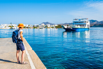 Youung woman tourist with backpack looking at ferry from Kimolos arriving in Pollonia port, Milos...