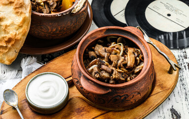 Baked mushrooms with onions in clay pot with sour cream on wooden board. Homemade food, close up