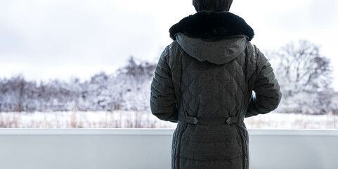 Back of person in dark grey winter coat with black fur hoodie standing and looking at the white snow landscape view in winter, depth of field. Panorama scene of beauty in nature scenic on freezing day