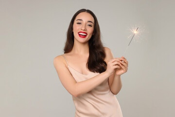Christmas celebration. Beautiful young woman with sparkler on grey background