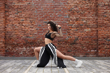 Beautiful young woman dancing hip hop near brick wall outdoors