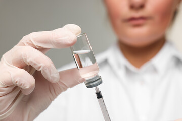 Doctor filling syringe with medication from glass vial on grey background, closeup