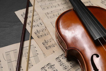 Violin, bow and music sheets on black table, closeup