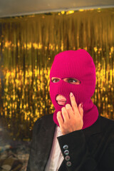 A young woman in a pink balaclava looks in the mirror