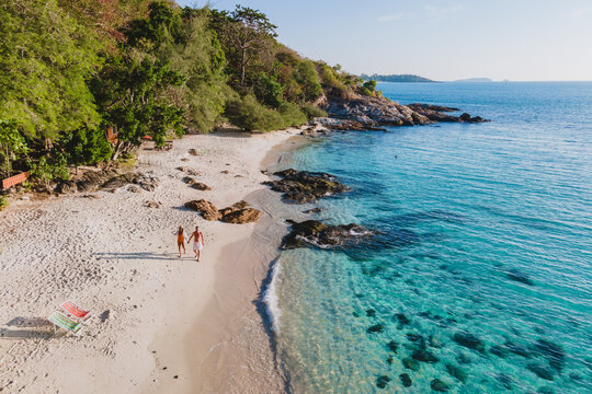 Koh Samet Island Thailand, aerial drone view from above at a couple of men and woman walking on the beach of Samed Island in Thailand with a turqouse colored ocean and a white tropical beach
