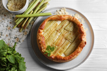 Freshly baked rhubarb pie and stalks on white wooden table, flat lay
