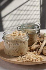 Platter with tasty prepared horseradish and roots on white wooden table