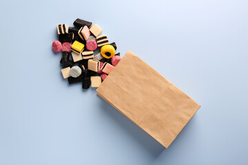 Paper bag with tasty liquorice candies on light blue background, top view