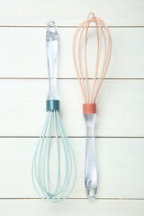 Two whisks on white wooden table, top view