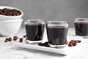 Glasses of coffee liqueur and beans on white marble table, closeup