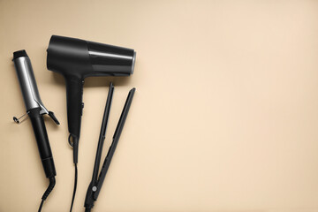 Curling iron, straightener and hair dryer on beige background, flat lay. Space for text