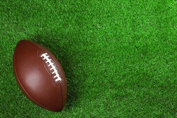 American football ball on green grass, top view. Space for text