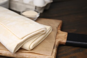 Raw puff pastry dough on wooden table, closeup