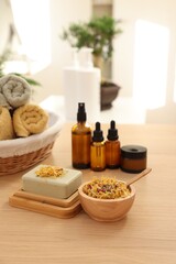 Soap bar, dry flowers, bottles of essential oils, jar with cream and towels on wooden table indoors. Spa time