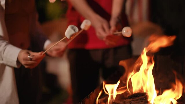 Close-up. People in their hands hold sticks with marshmallows in a flame on a fire. Leisure concept for the holidays