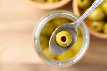 Pickled olives, Pitted green olives in glass jar with spoon, Table top view