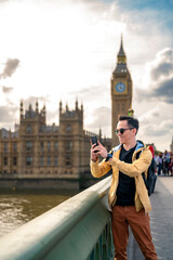 Young happy Latin man tourist wearing sunglasses and casual outfit holding smartphone while taking...