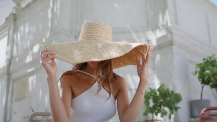Sexy woman touching straw hat posing with gentle smile at sunlight cafe portrait
