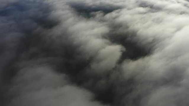 Flying over bright white clouds and dark mysterious land in shadow below
