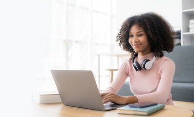 African American girl in headphones watching video lesson on computer in living room at home, happy...