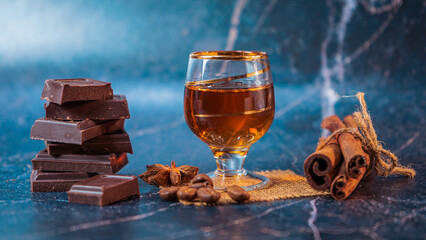 A glass of cognac and pieces of chocolate on a dark background. Glass of brandy on a old wooden table with a  chocolate, cinnamon sticks. selective focus.