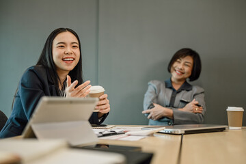 Cheerful Asian female manager talking to colleagues during break at meeting room.