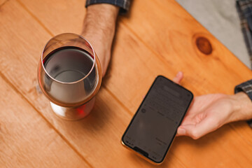 Close-up shot of a man with a glass of wine and holding a phone to track amount of alcohol or to...
