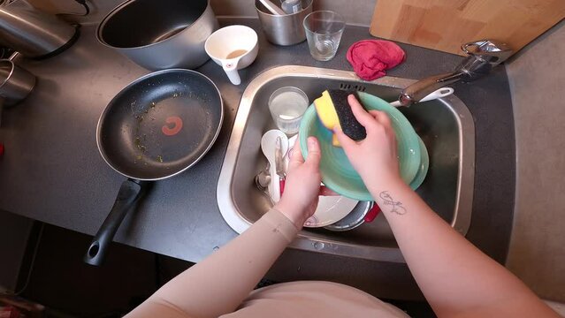 Dishwashing. POV camera woman hand washing full sink of dishes in kitchen. Household chores. Concept of housekeeping and washing dishes. Standpoint POV of person washed utensils in sink home kitchen. 